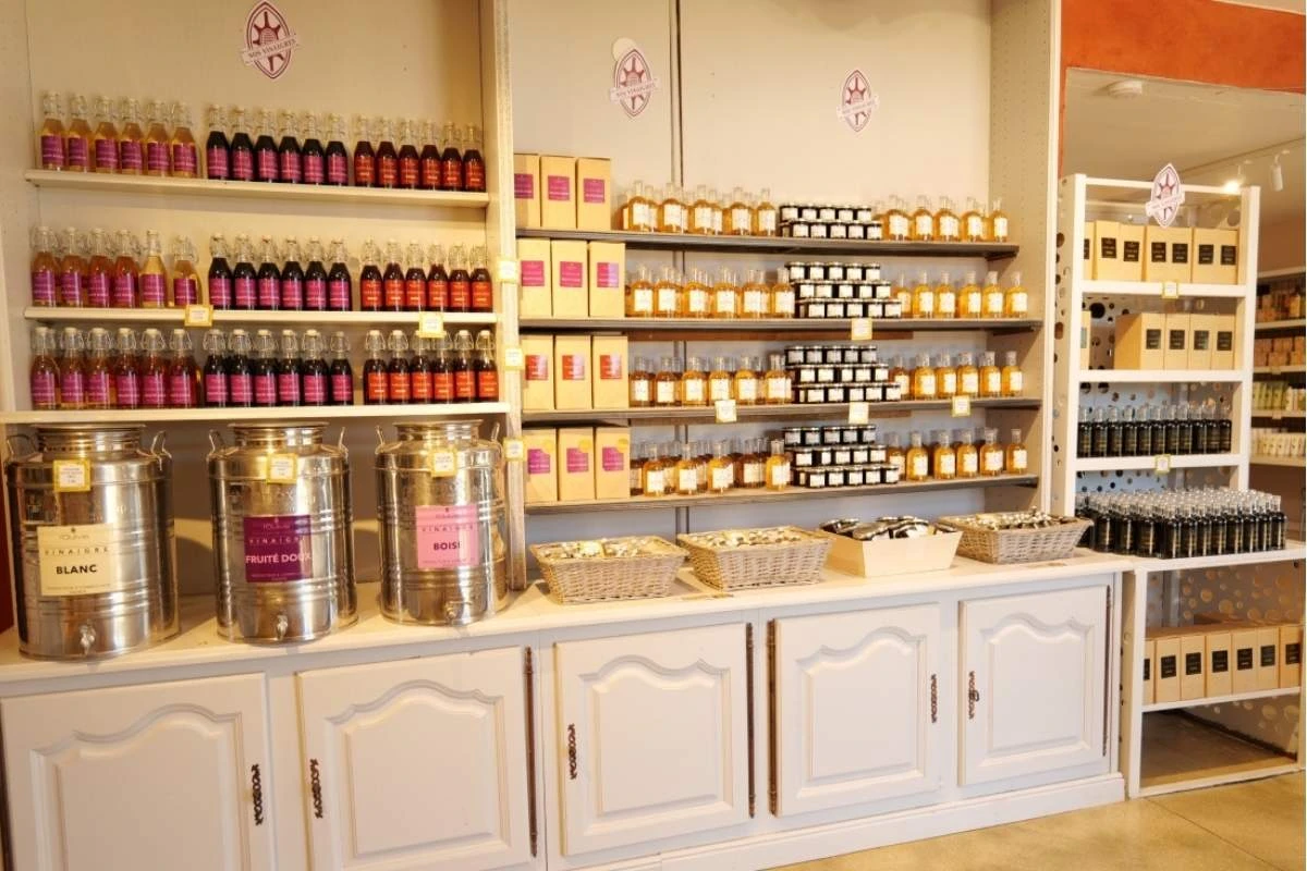 Rayons du magasin de l'Oulivie avec des bouteilles de vinaigre artisanal et de grosses cuves en inox pour la vente de produits du terroir